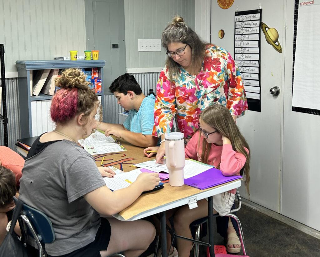 A teacher leaning over a table of students at work in a classroom