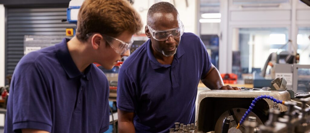 An experienced worker showing an apprentice how to use a machine