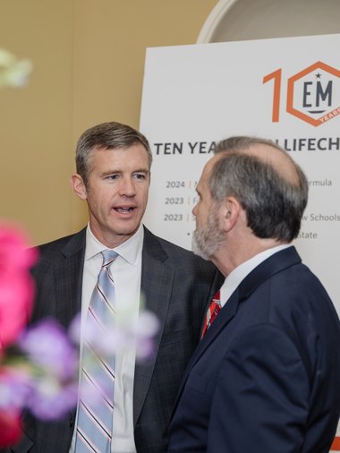 Two men talking in front of a board marking ten years of Empower Mississippi