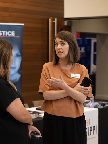 A woman in an orange top in conversation beside Empower Mississippi banners
