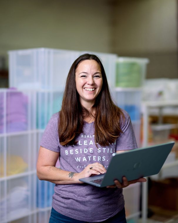 A woman holding a laptop in a production room lined with storage crates