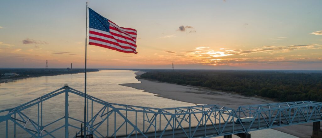An American flag flying above a bridge across the Mississippi River at sunrise