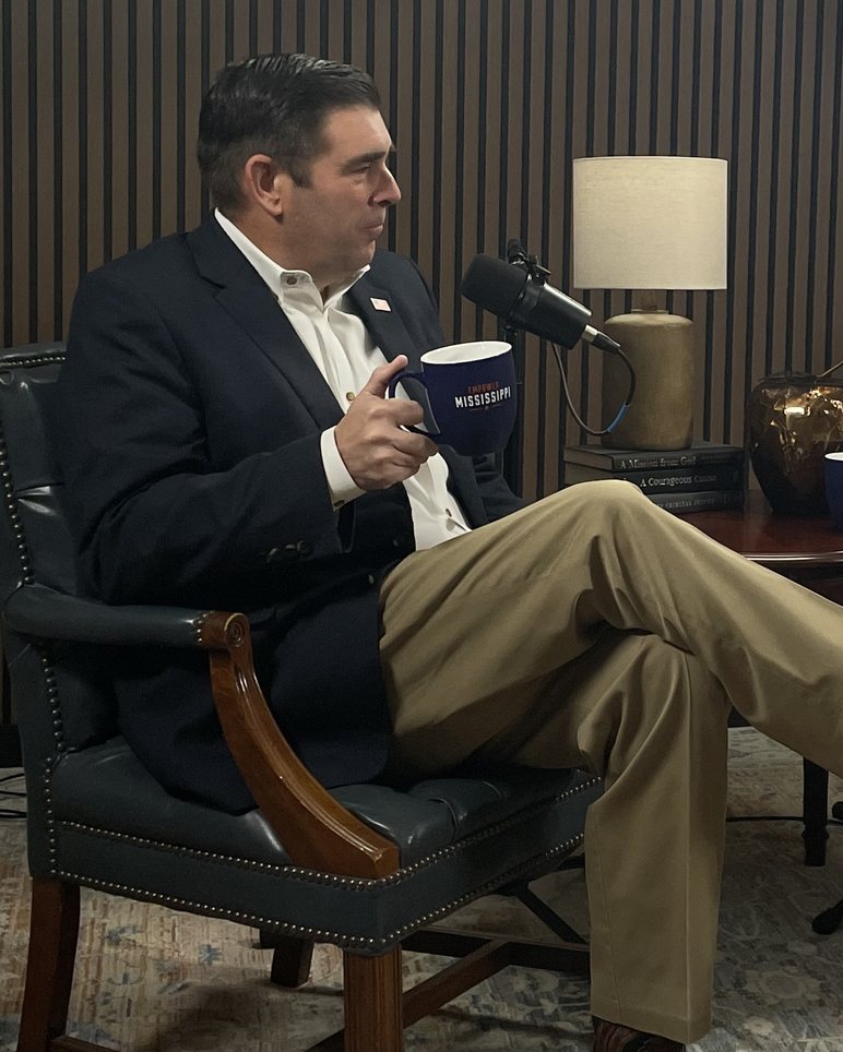 A man seated in an armchair speaking into a microphone in the Empower podcast studio