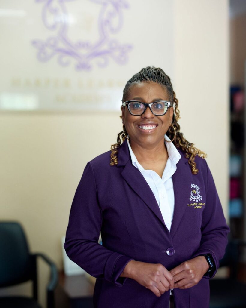 A woman in a purple school blazer standing in front of the academy crest