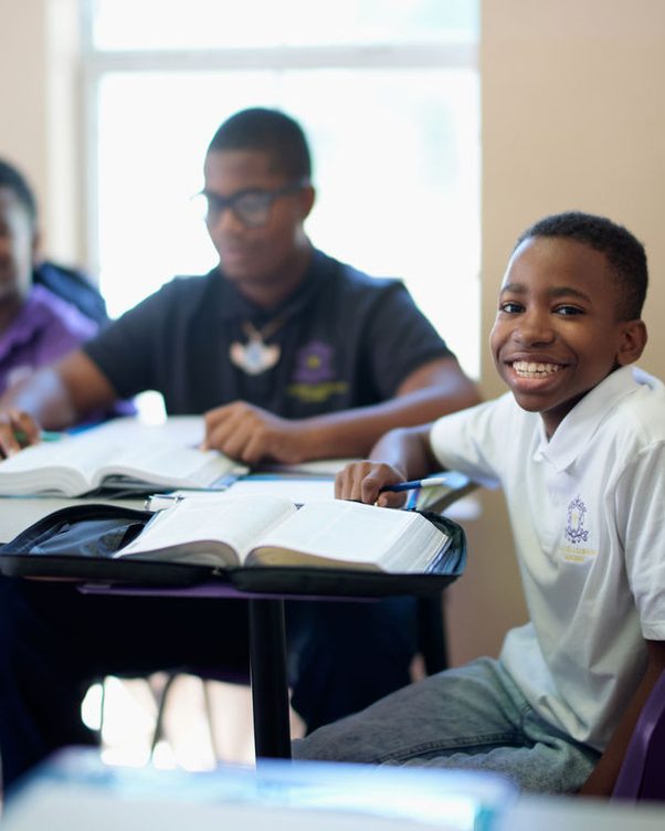 Students working at desks in a classroom, one of them smiling towards the camera