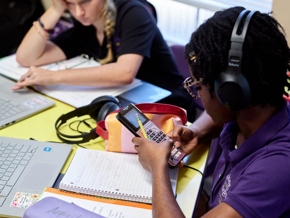 Two students working at laptops and notebooks in a classroom