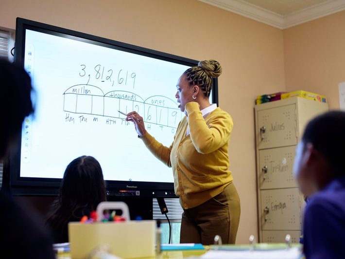 A teacher working through a maths problem on a smartboard with her class
