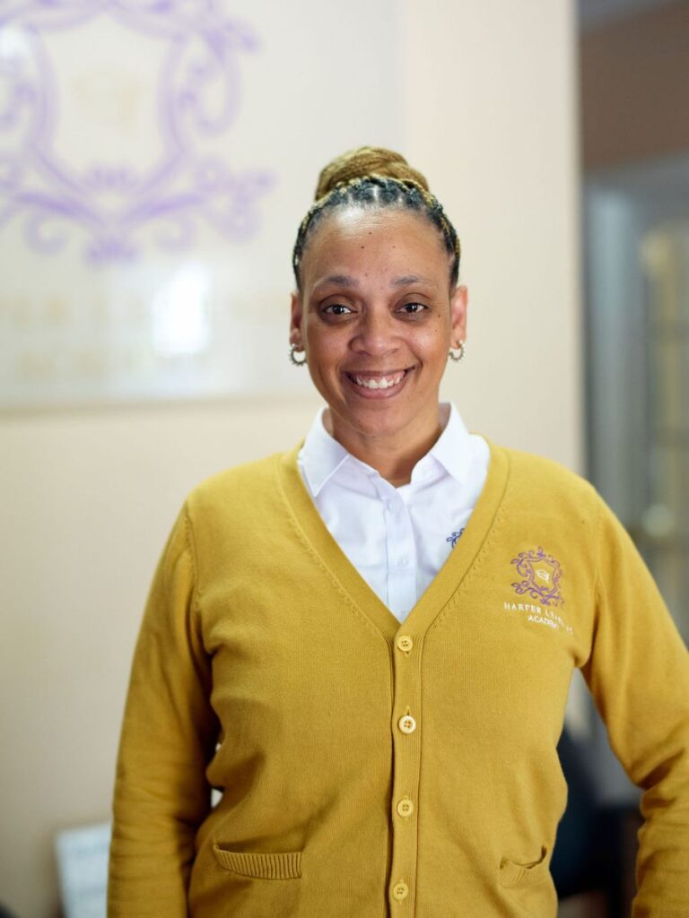 A teacher in a yellow cardigan standing in a school corridor