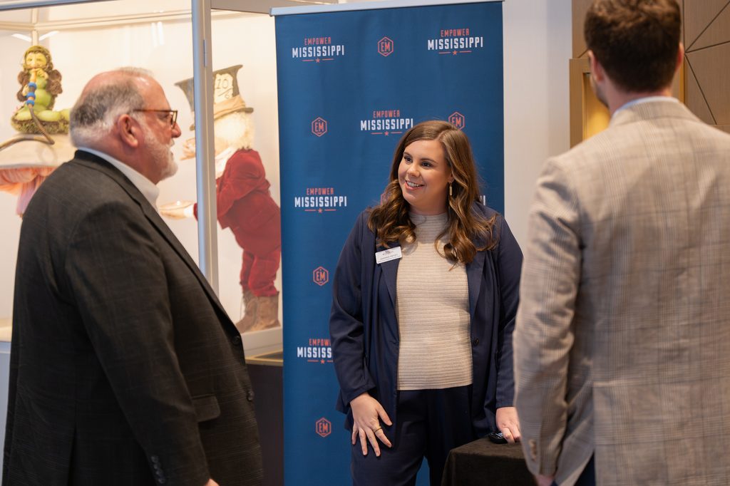 Three people talking in front of an Empower Mississippi banner at an event