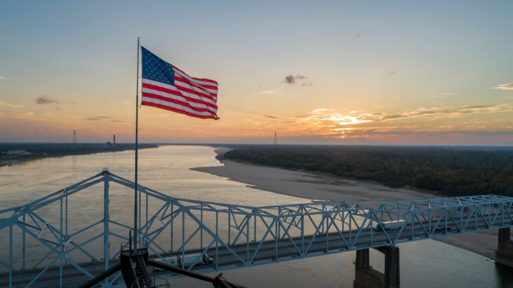 An American flag flying above the old Highway 80 bridge over the Mississippi River at Vicksburg, at sunrise