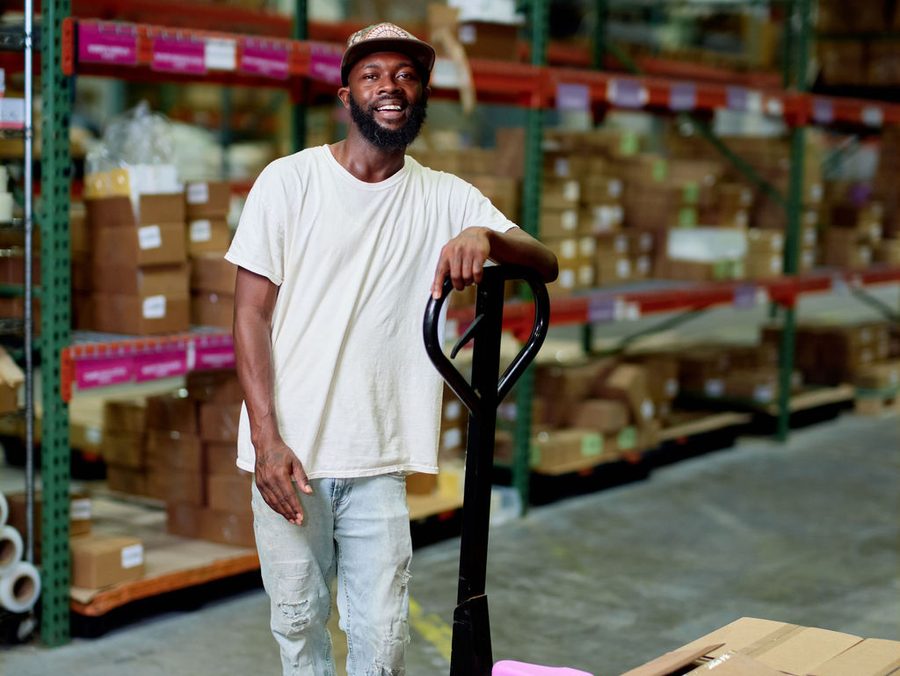A man standing with a pallet truck between warehouse racks