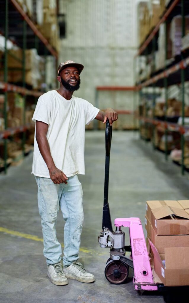 A man standing with a pallet truck in a warehouse aisle